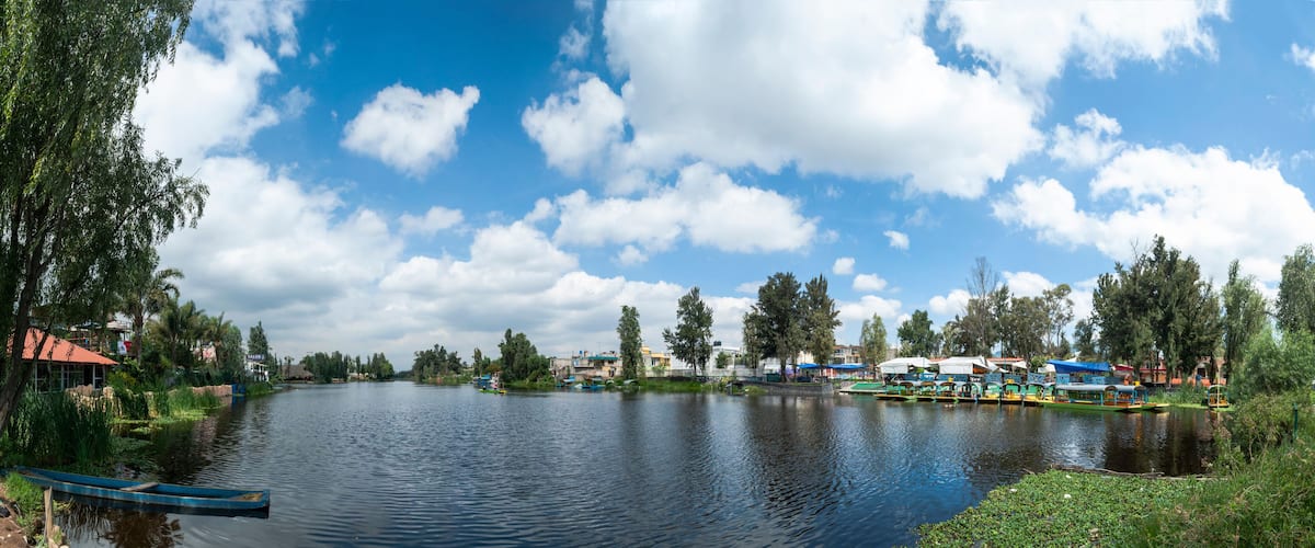 A calm river with boats, trees, and buildings along the banks.