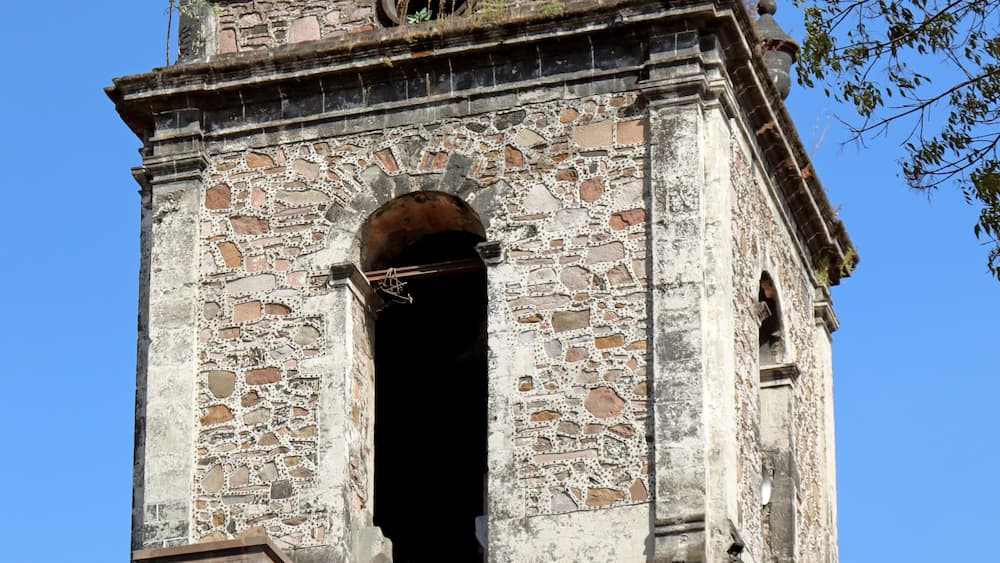 Ein historischer Stein-Glockenturm mit rotem Dach und einem Kreuz auf der Spitze.