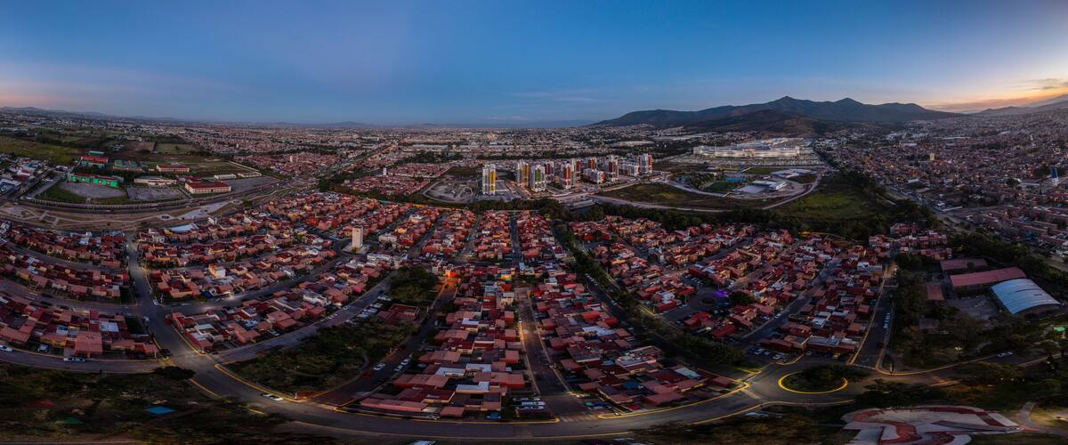 An aerial view of a city with dense housing, a large industrial area, and mountains in the background.