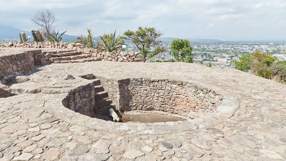An ancient stone structure with a circular well, surrounded by a stone wall and steps leading up to it.