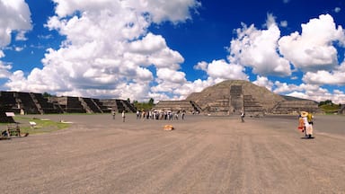 Una gran pirámide antigua de cima plana, rodeada de estructuras más pequeñas y un cielo azul despejado con nubes.