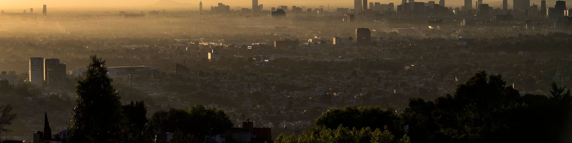 Panoramic view of Mexico City at dawn, with fumarole of active volcano Popocatepetl beside Iztaccihuatl, mist between skyscrapers