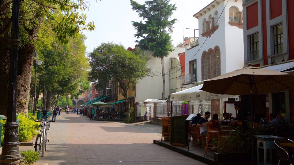 A tree-lined street with outdoor cafes and shops.