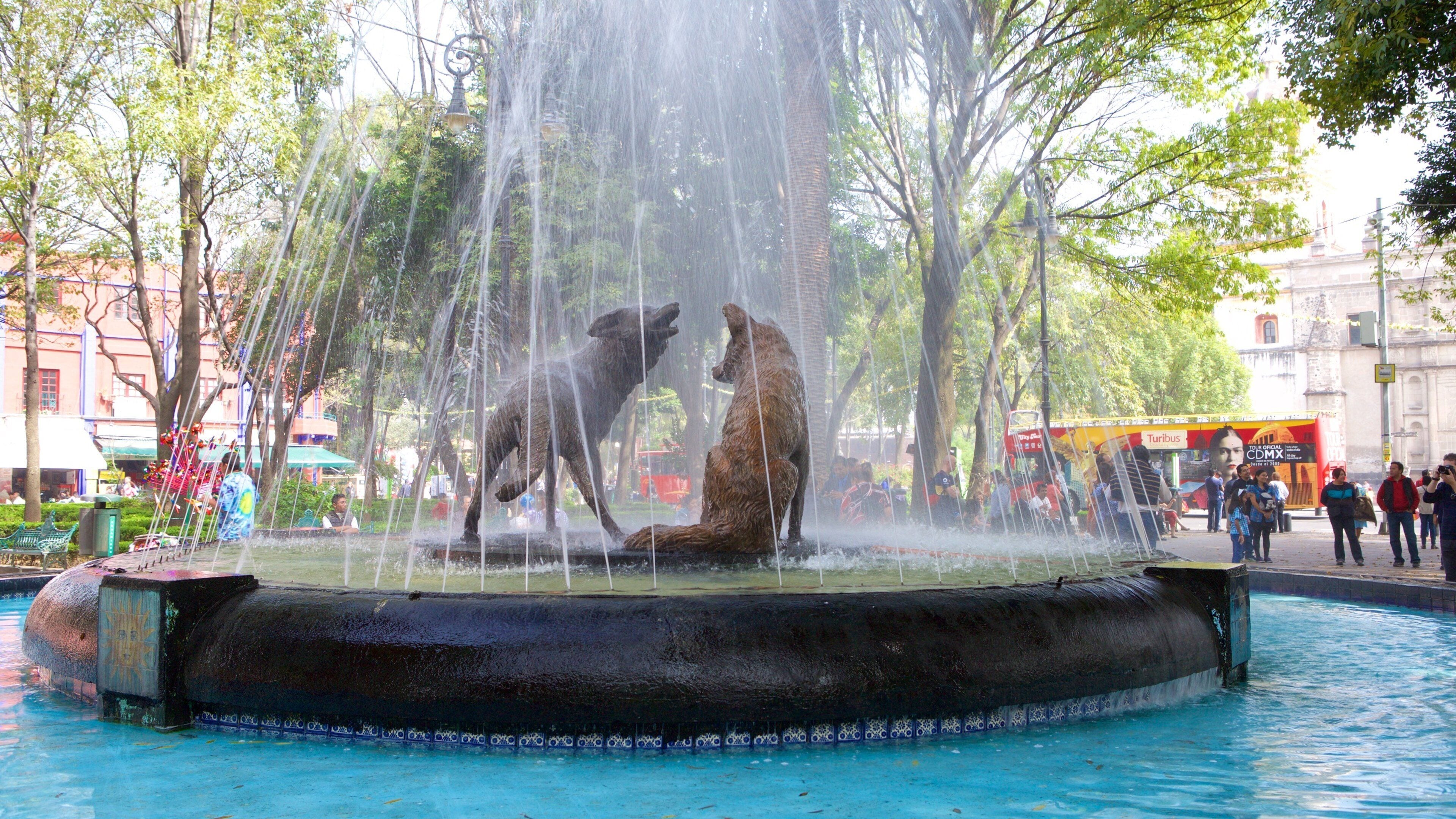 A fountain with two bear statues in the center, surrounded by trees and a cityscape in the background.