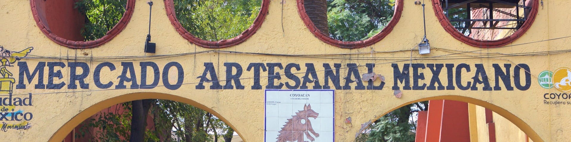 An entrance to Mercado Artesanal Mexicano with colorful decorations and a sign featuring a coyote.