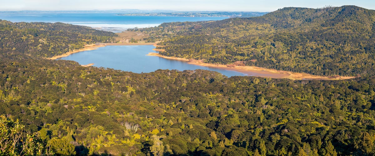 A coastal landscape with a large lake surrounded by dense forest and hills.