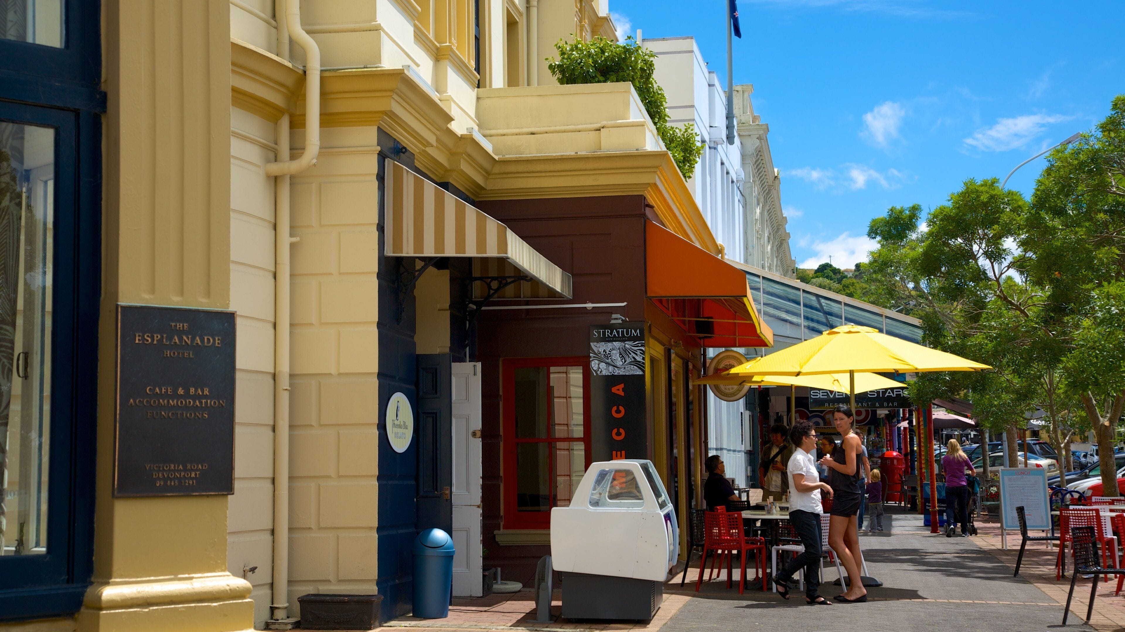A street with outdoor seating at a cafe and bar, a vintage car, and a building with a sign for The Esplanade Hotel.
