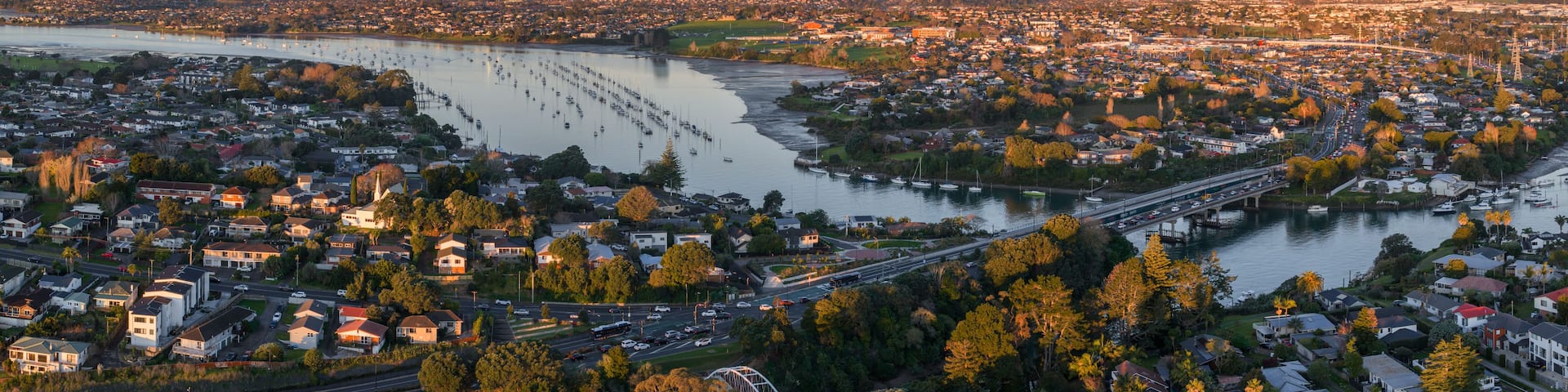 A coastal cityscape with a river, marina, and a bridge.