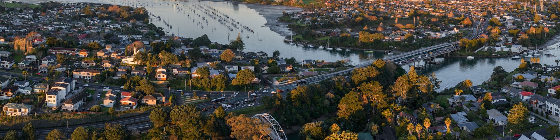A coastal cityscape with a river, marina, and a bridge.