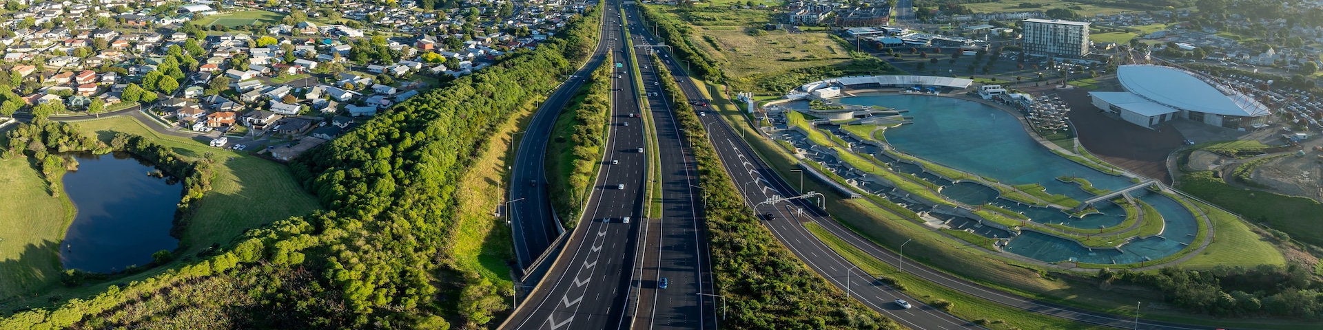 Eine Autobahn mit mehreren Fahrspuren, umgeben von Wohngebieten, einem großen Gewässer und einem Gebäudekomplex.
