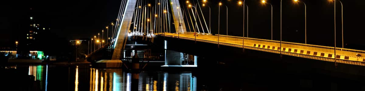 A lit cable-stayed bridge at night with its reflection in the water.