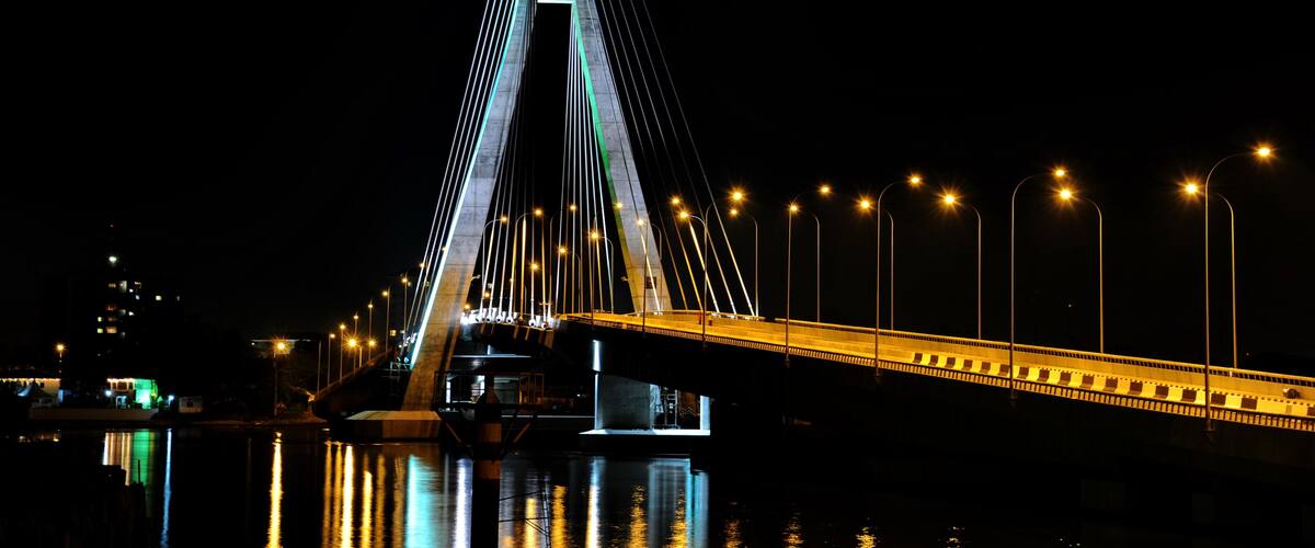 A lit cable-stayed bridge at night with its reflection in the water.