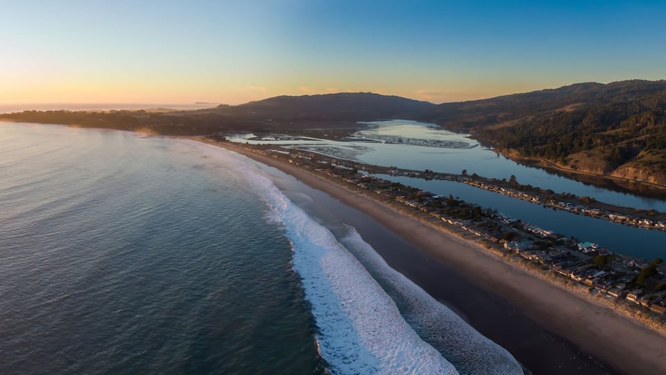 A coastal landscape with a beach, a river, and hills in the background.