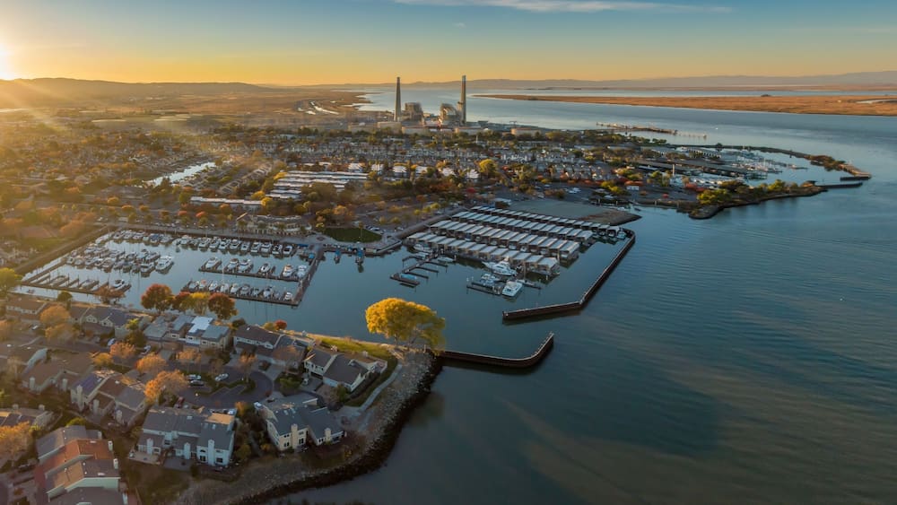 Aerial view of Pittsburg, California, USA, at sunset. The image shows the city's marina, waterfront homes, and a power plant in the distance.