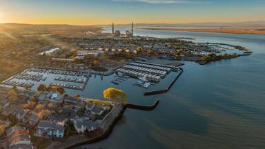 Aerial view of Pittsburg, California, USA, at sunset. The image shows the city's marina, waterfront homes, and a power plant in the distance.