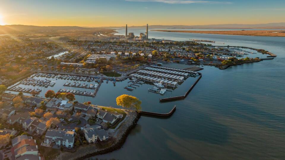 An aerial view of a coastal city with a marina, residential areas, and a large industrial facility.