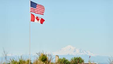 Two flags on a flagpole, with a snow-capped mountain in the background.