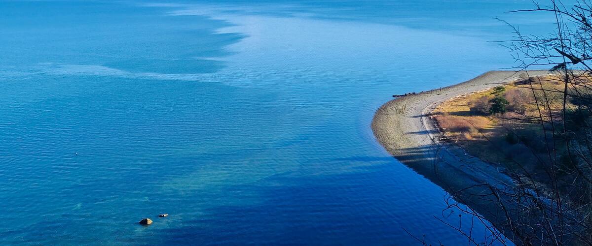 Et kystlandskab med et klart, blåt hav, en sandstrand og fjerne bjerge.