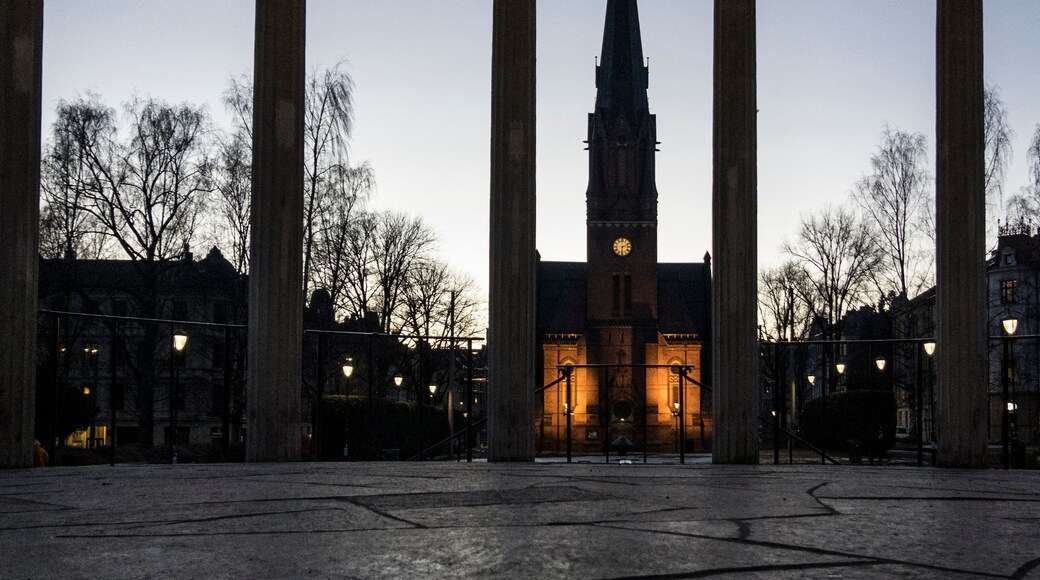 A large open plaza with a central building featuring a tall spire and clock.