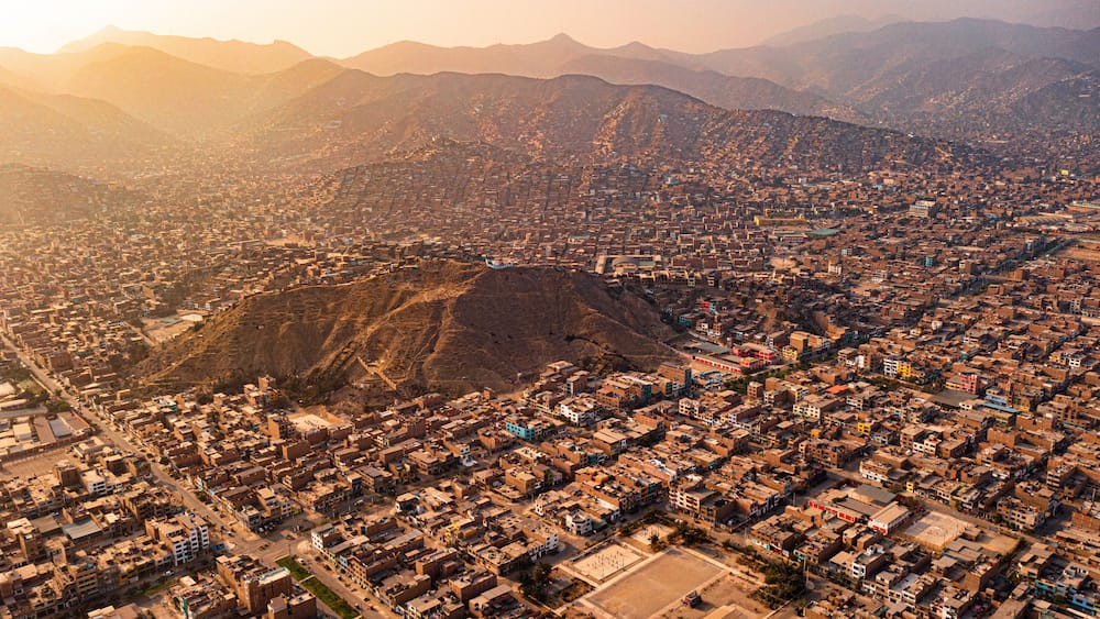 An aerial view of a city with a prominent hill in the center, surrounded by densely packed buildings and mountains in the background.