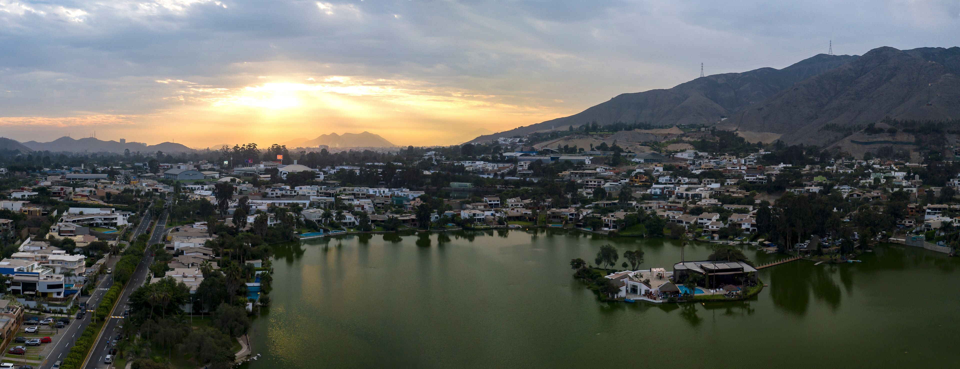 A cityscape with a lake, mountains, and a sunset.