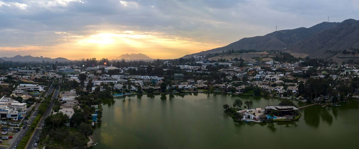 A cityscape with a lake, mountains, and a sunset.