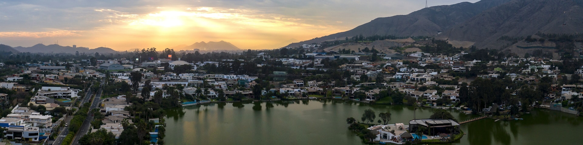 A cityscape with a lake, mountains, and a sunset.