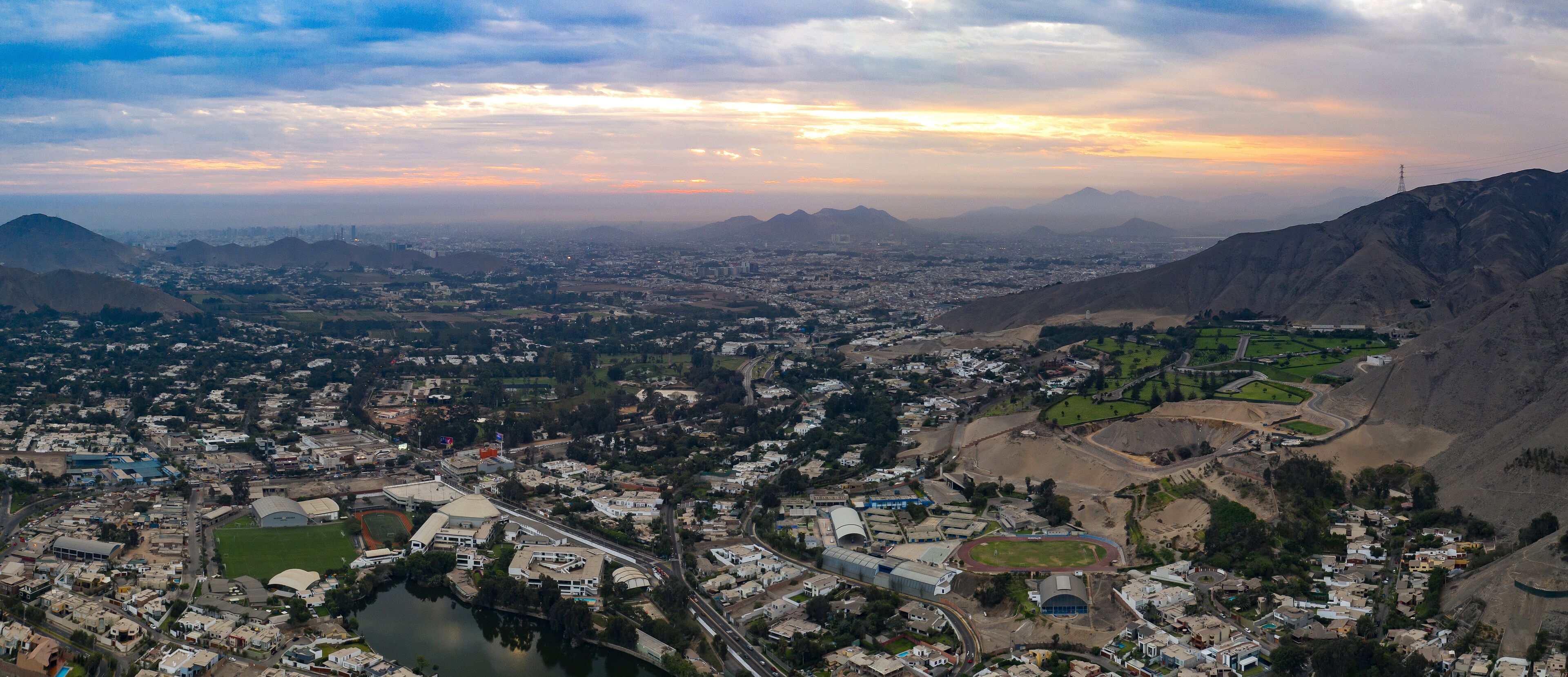 Lima, Perú - May 4 2019:  Panoramic aerial view of La Molina district in La Planicie urbanization. Cityscape with lake at sunset. Urban panorama in Lima city.