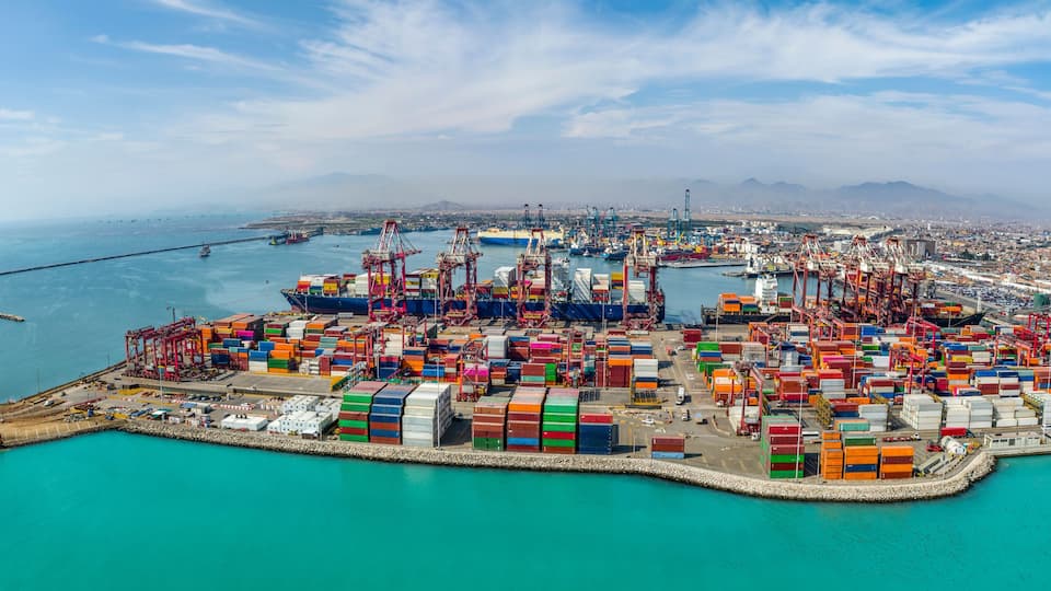 A bustling port with numerous colorful shipping containers, a large cargo ship, and a distant cityscape.