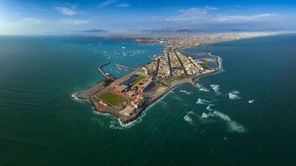 An aerial view of a coastal city with a prominent peninsula featuring a fortified structure and a dense urban area.