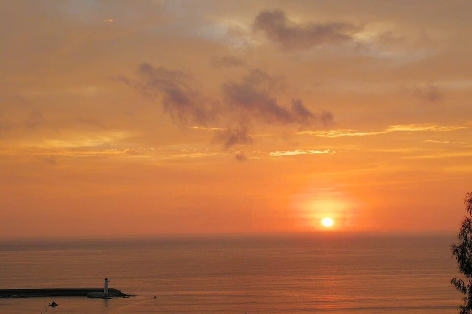 A sunset over a calm sea with a lighthouse and a pier.