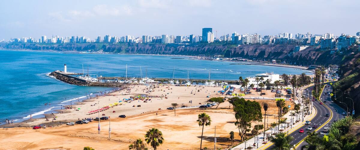 A coastal cityscape with a beach, a lighthouse, and a dense urban skyline.