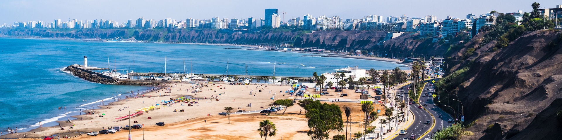 A coastal cityscape with a beach, a lighthouse, and a dense urban skyline.