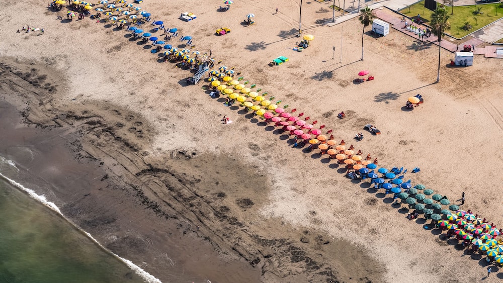 An aerial view of a beach with rows of colorful umbrellas and beach chairs.