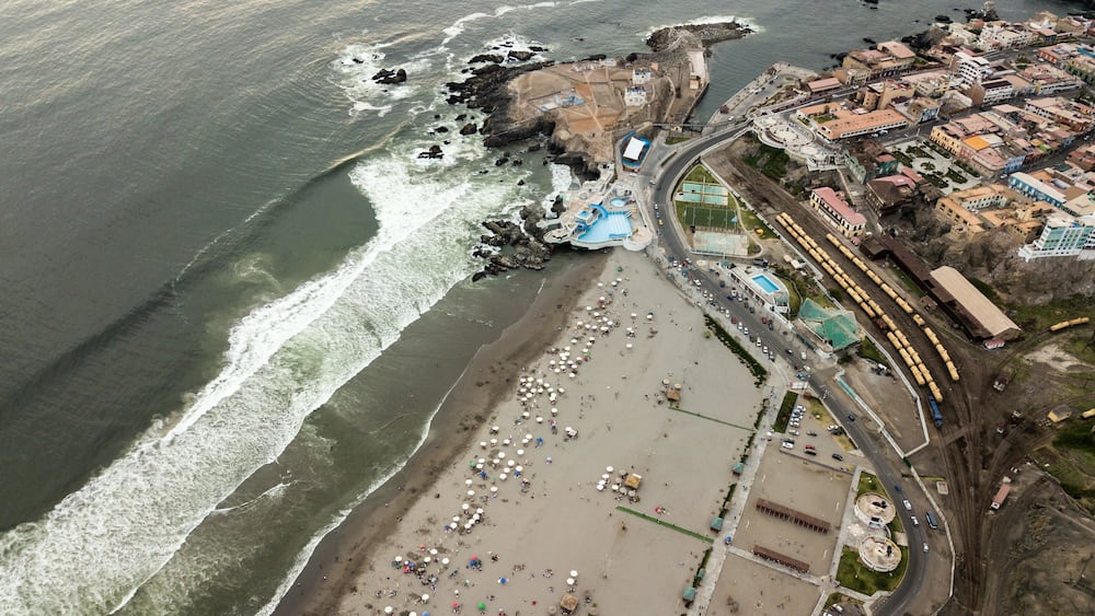An aerial view of a coastal town with a beach, rocky coastline, and a train station.