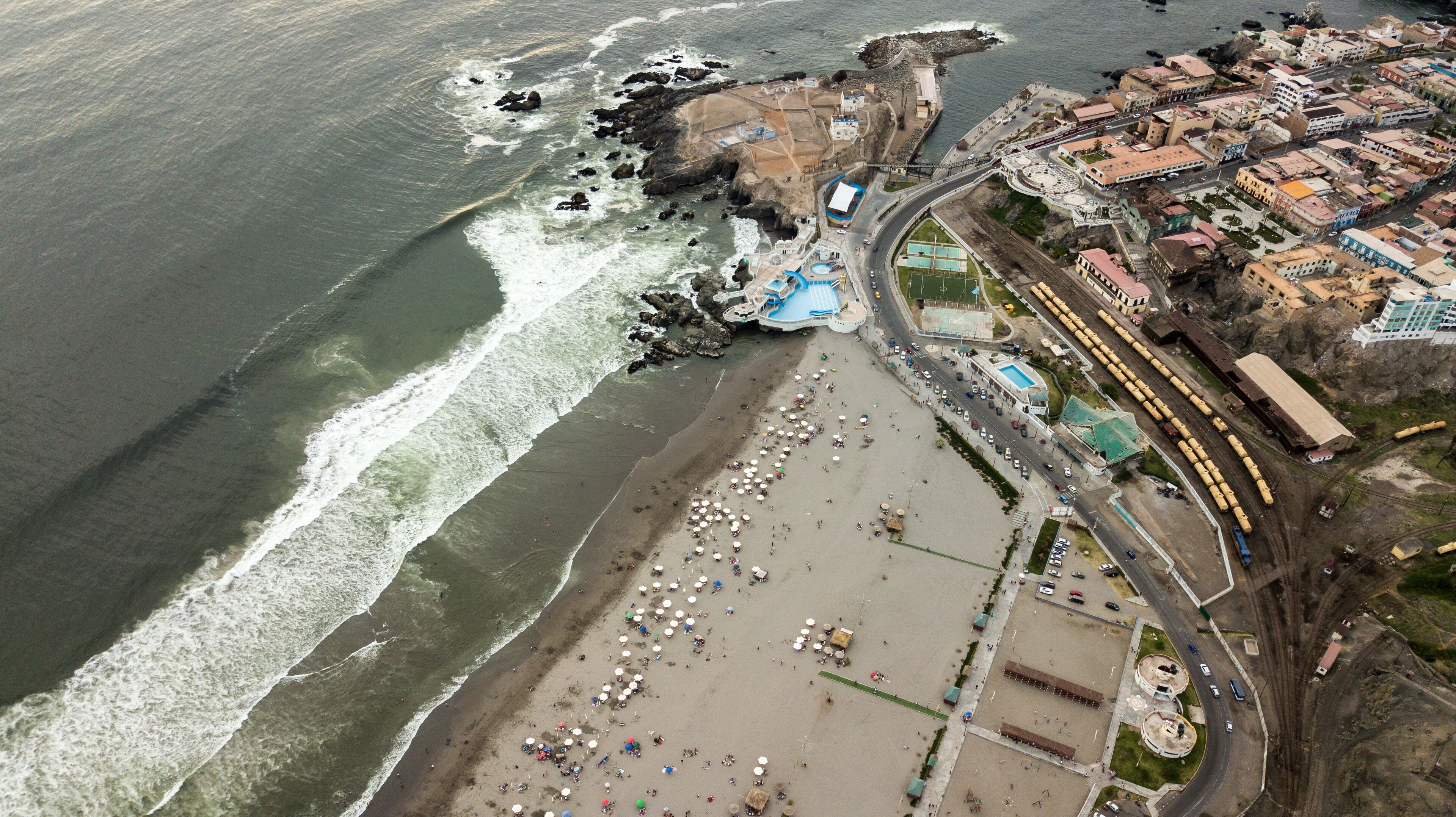 An aerial view of a coastal town with a beach, rocky coastline, and a train station.