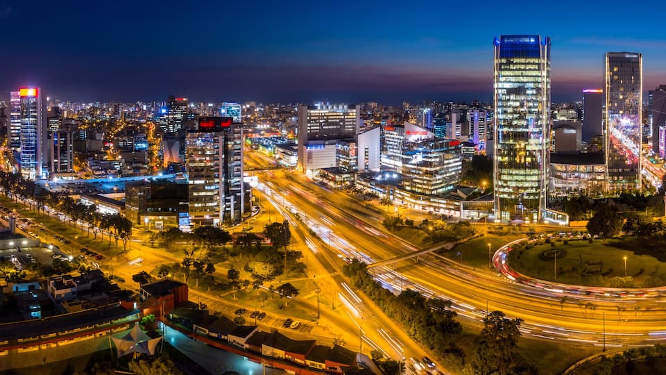 A cityscape at night with illuminated skyscrapers, busy highways, and a clear sky.