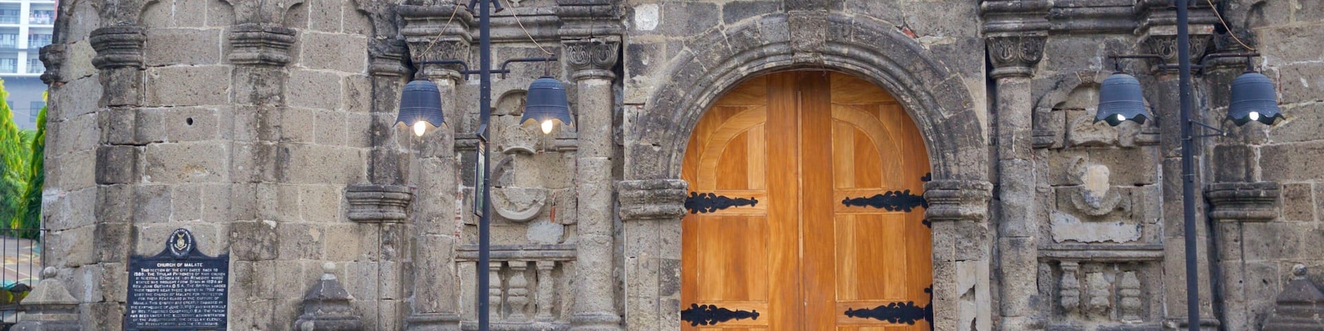 A historic stone building with a large wooden door, intricate carvings, and a plaque.