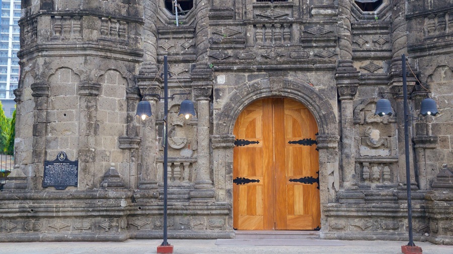 A historic stone building with a large wooden door, intricate carvings, and a plaque.