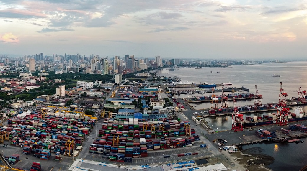 Ein geschäftiger Hafen mit zahlreichen Containern, einer weiten Wasserfläche und einer Stadtkulisse im Hintergrund.