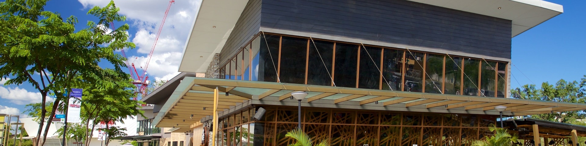 A modern building with a sloped roof and large windows, surrounded by greenery and a clear blue sky.