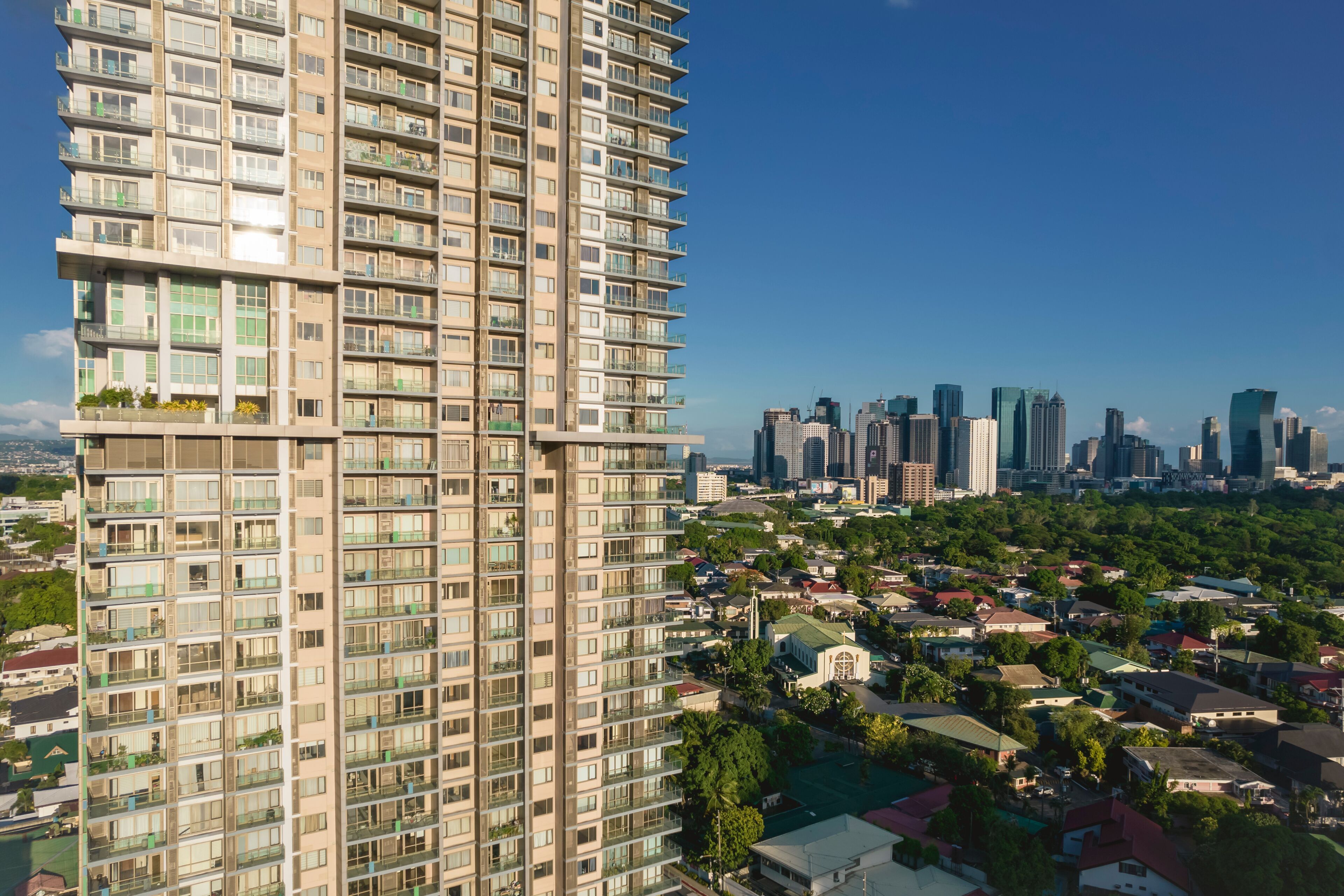 Un edificio alto con múltiples balcones, un denso horizonte urbano y una combinación de edificios residenciales y comerciales.