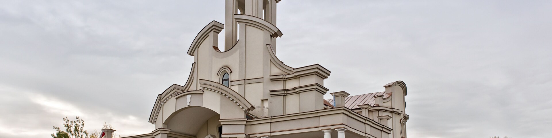 Uma igreja branca grande com uma alta torre de sino e uma cruz no topo.