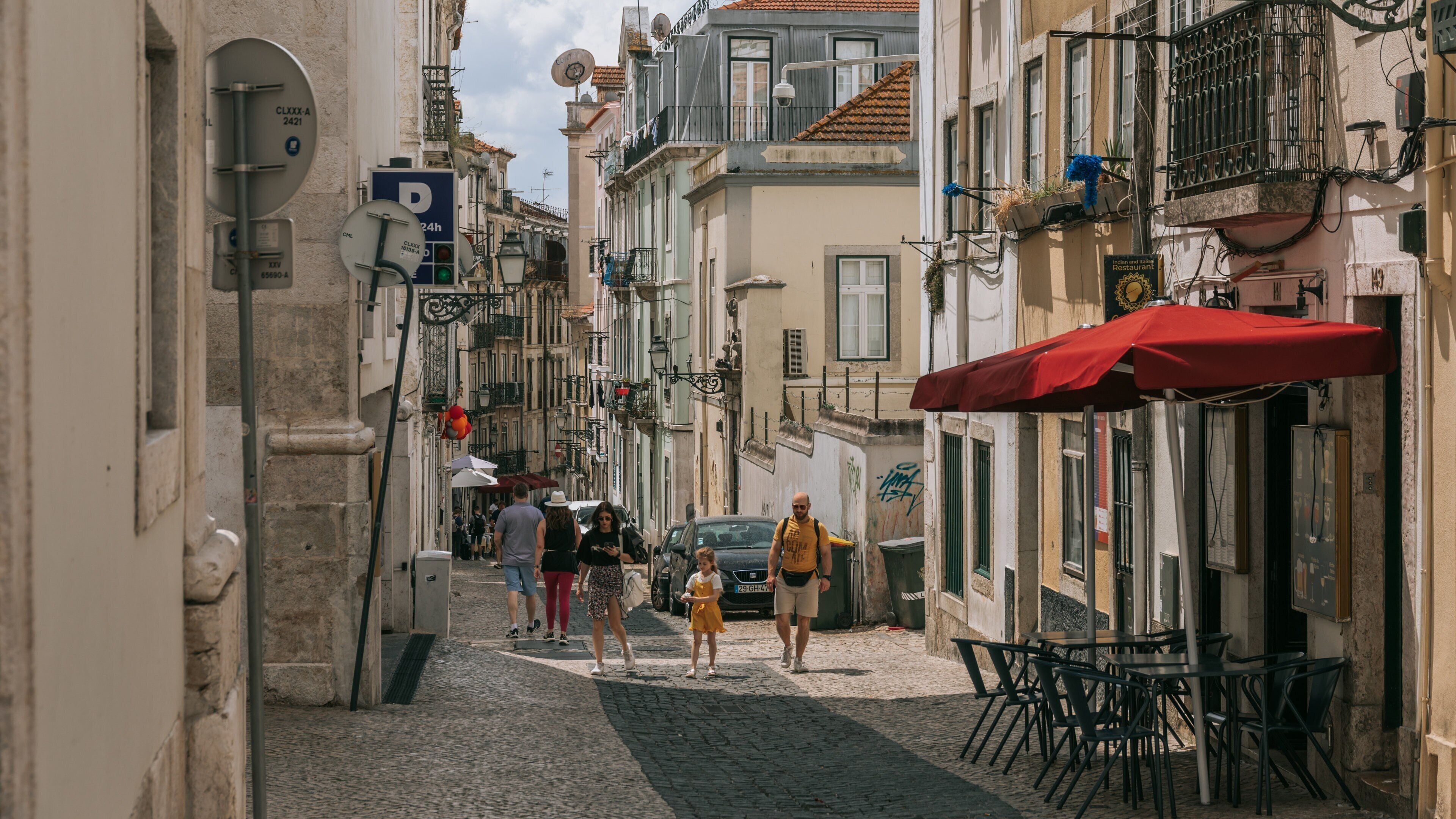A narrow cobblestone street lined with historic buildings, a red umbrella, and outdoor seating.