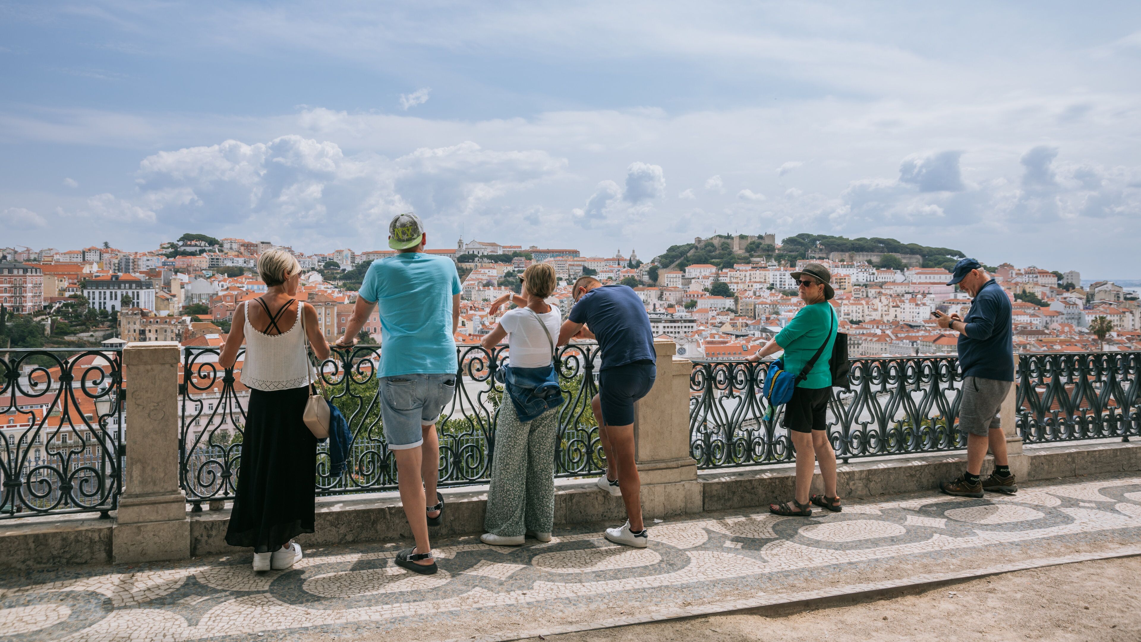 A group of people on a bridge overlooking a cityscape with historic buildings and a hill in the background.