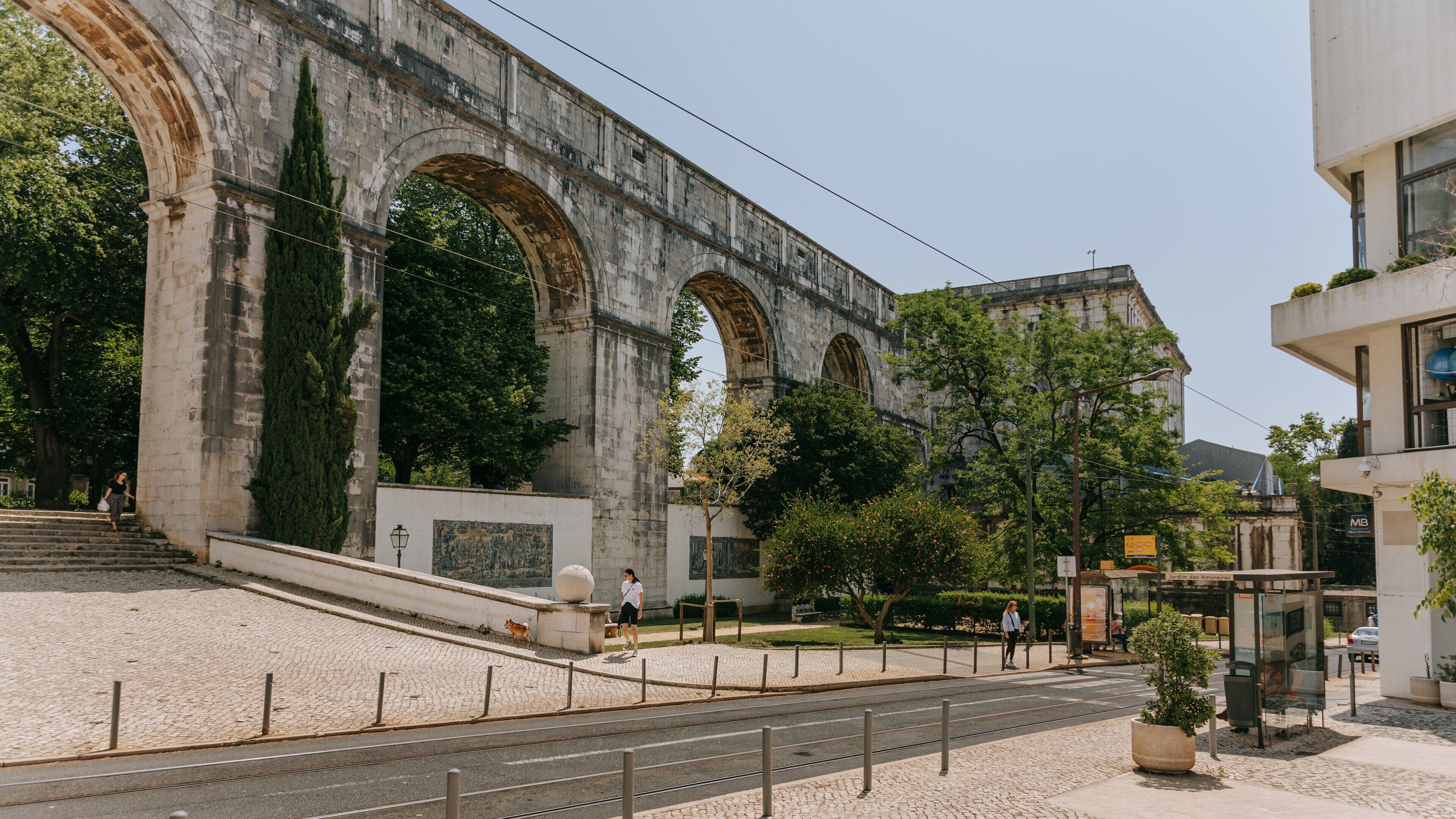 Un puente de piedra histórico con arcos, una línea de tranvía y un edificio moderno con un letrero.