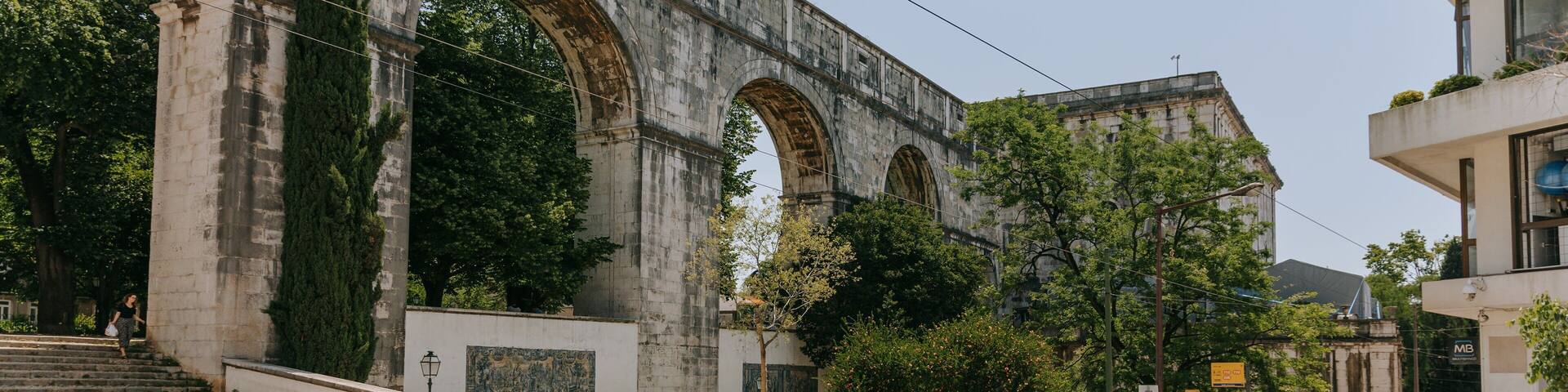 A historic stone bridge with arches, a tram line, and a modern building with a sign.