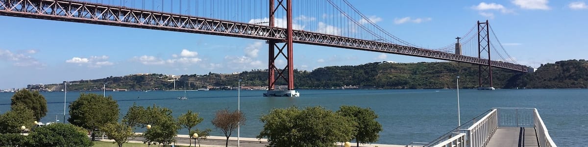 A large suspension bridge over a body of water with a park and railway tracks in the foreground.