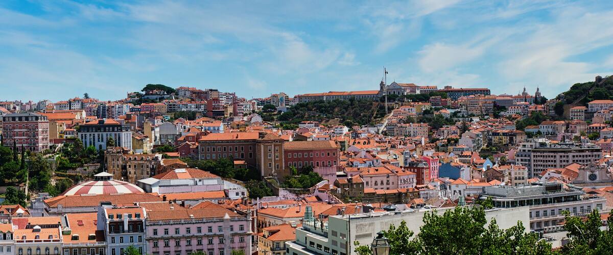 A densely packed cityscape with historic buildings and a prominent hill with a church.