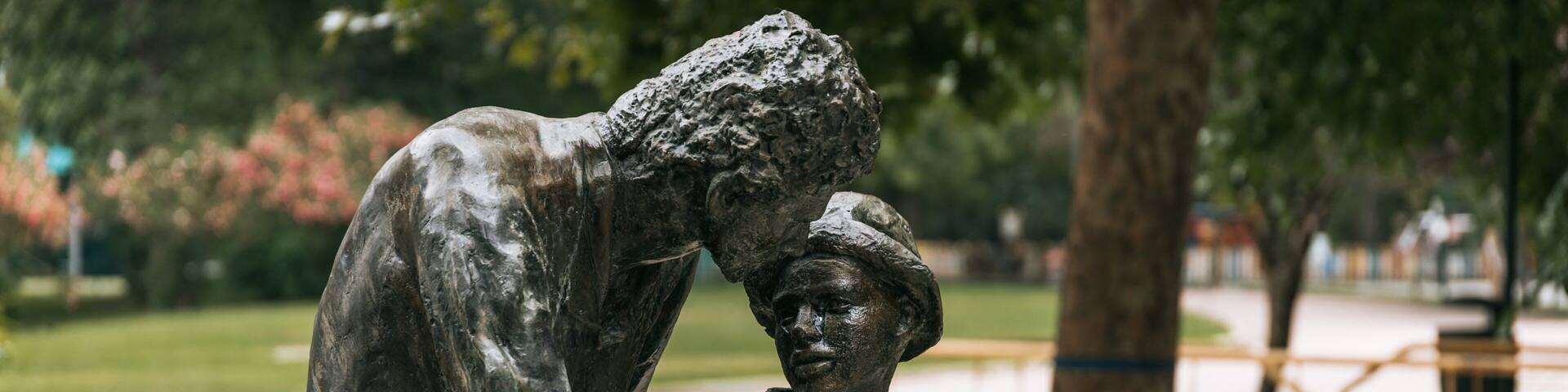 A statue of a person helping another on a bicycle in a park.
